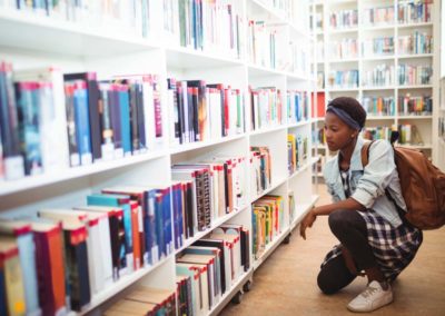 student selecting book from book shelf in library at school