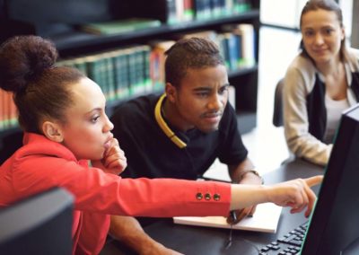 Small group of university students working on computer in a library. Young people finding information for their college assignment.